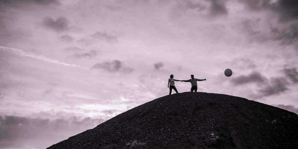 Deux personnes avec ballon sur colline sombre.
