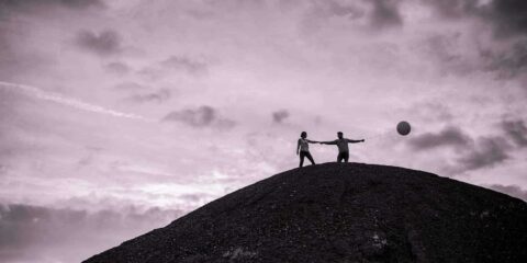 Deux personnes avec ballon sur colline sombre.
