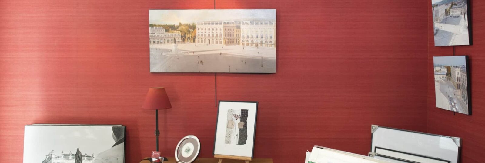 Salle d'exposition avec plusieurs tableaux sur murs rouges.