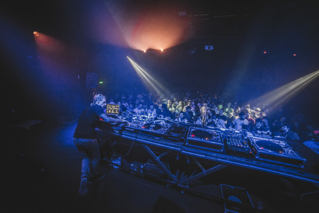 Scène de DJ en pleine performance lors d’une soirée Techno Story, éclairages intenses et foule animée.