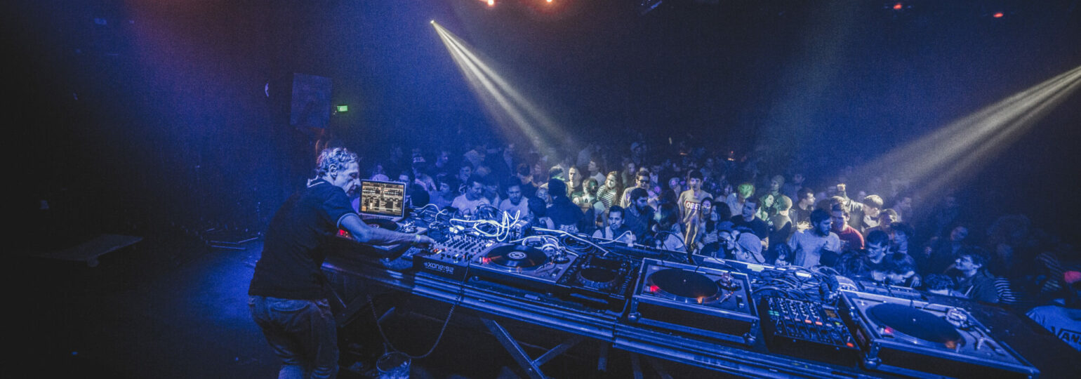 Scène de DJ en pleine performance lors d’une soirée Techno Story, éclairages intenses et foule animée.