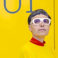Personne en lunettes blanches sur fond jaune vif.