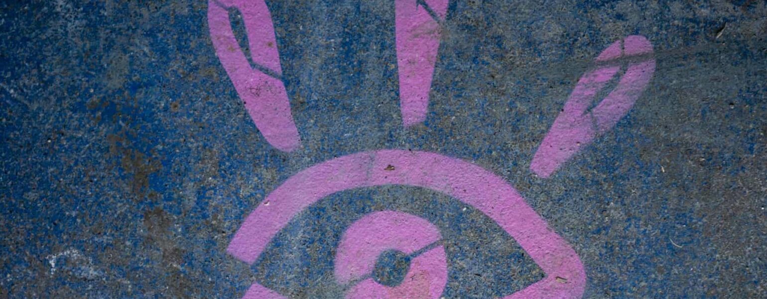 Graffiti œil rose sur mur bleu.