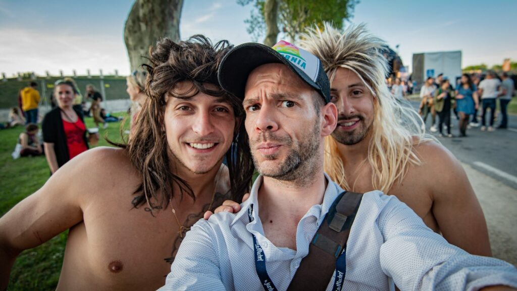 Trois hommes souriants prennent un selfie en extérieur.