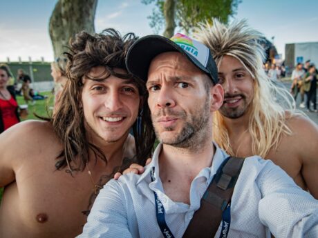 Trois hommes souriants prennent un selfie en extérieur.