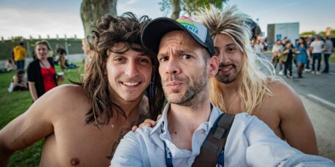 Trois hommes souriants prennent un selfie en extérieur.
