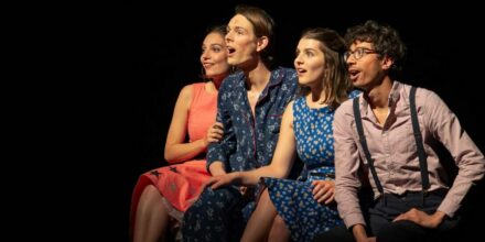 Quatre personnes souriantes sur une scène de théâtre.