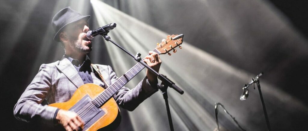 Homme jouant de la guitare sur scène illuminée.