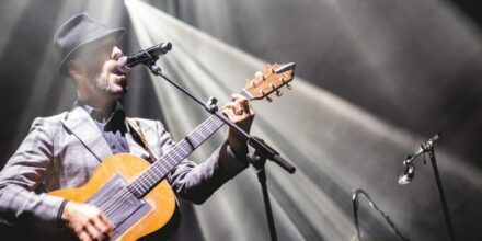 Homme jouant de la guitare sur scène illuminée.