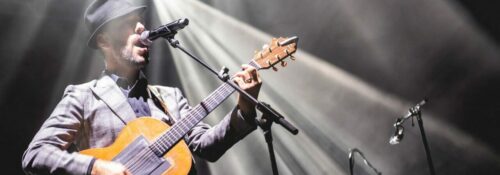 Homme jouant de la guitare sur scène illuminée.