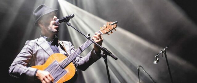 Homme jouant de la guitare sur scène illuminée.