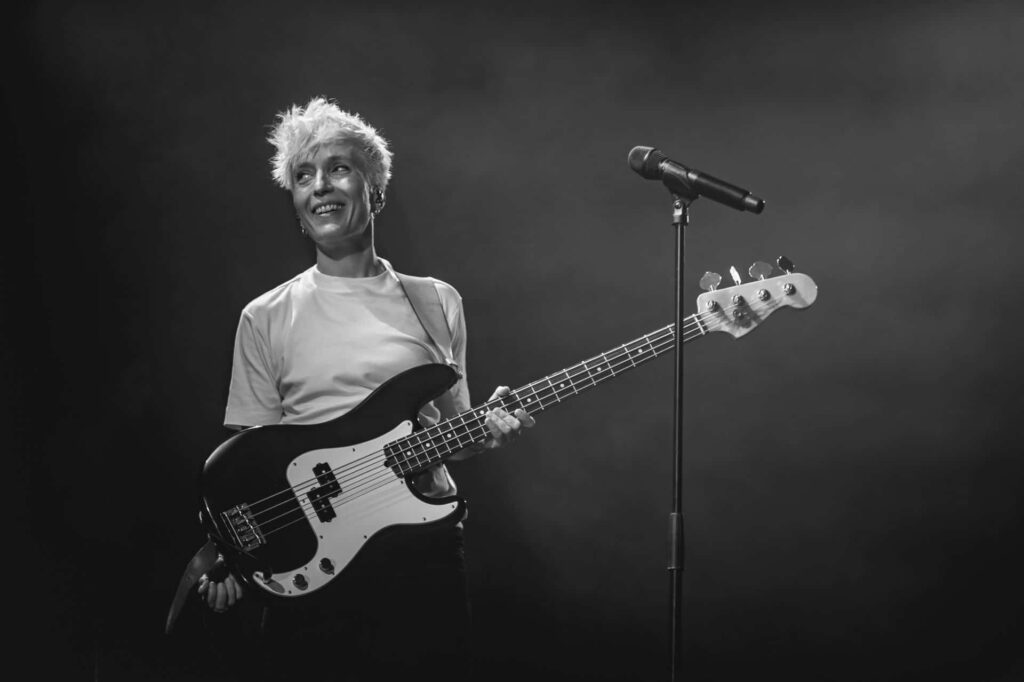 Musicienne souriante avec guitare basse sur scène.
