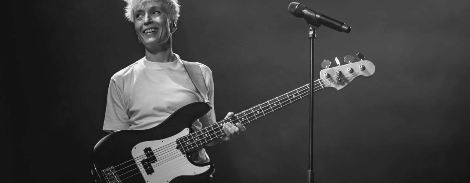 Musicienne souriante avec guitare basse sur scène.