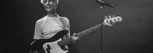 Musicienne souriante avec guitare basse sur scène.