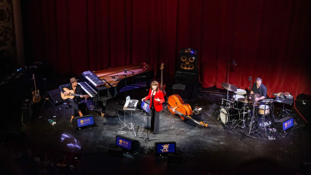 Concert avec musiciens sur scène, instruments variés.