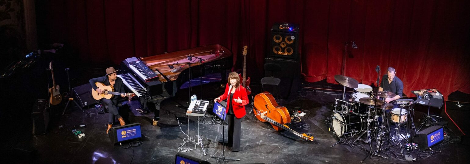 Concert avec musiciens sur scène, instruments variés.