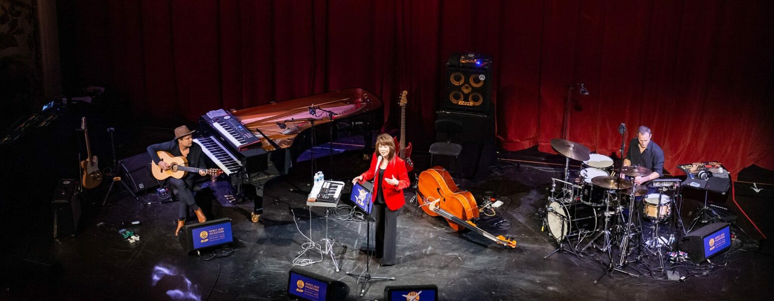 Concert avec musiciens sur scène, instruments variés.