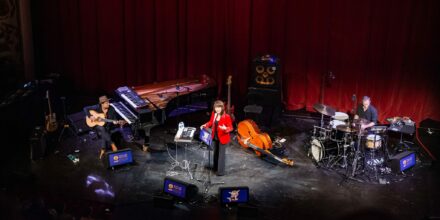 Concert avec musiciens sur scène, instruments variés.