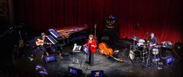 Concert avec musiciens sur scène, instruments variés.