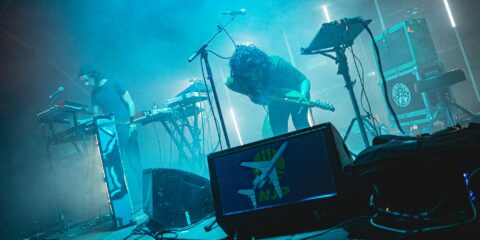 Concert avec synthétiseurs et guitare sur scène.