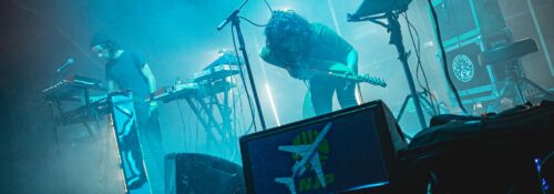 Concert avec synthétiseurs et guitare sur scène.