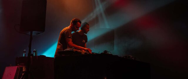 Deux DJ sur scène avec lumières colorées.