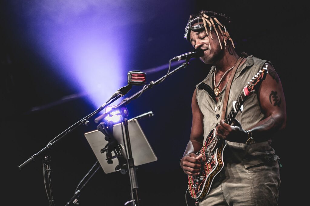 Artiste jouant de la guitare sur scène, éclairage violet.