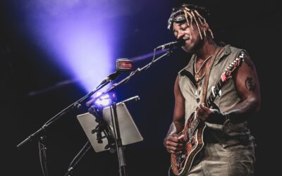 Artiste jouant de la guitare sur scène, éclairage violet.