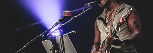 Artiste jouant de la guitare sur scène, éclairage violet.