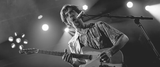 Homme jouant de la guitare sur scène.