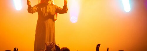 Artiste sur scène, éclairage coloré, public enthousiaste.