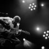 Musicien jouant de la guitare sur scène en noir et blanc.