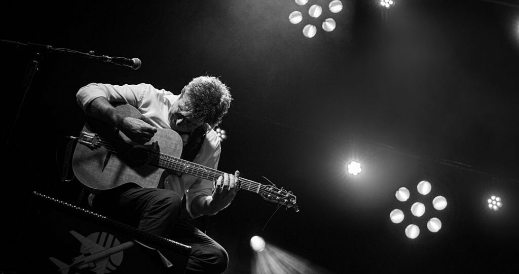 Musicien jouant de la guitare sur scène en noir et blanc.