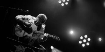 Musicien jouant de la guitare sur scène en noir et blanc.