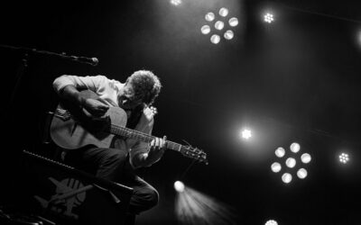 Musicien jouant de la guitare sur scène en noir et blanc.