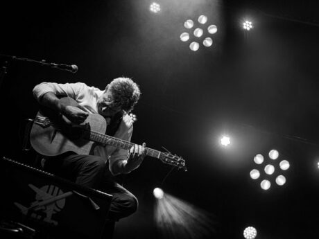 Musicien jouant de la guitare sur scène en noir et blanc.