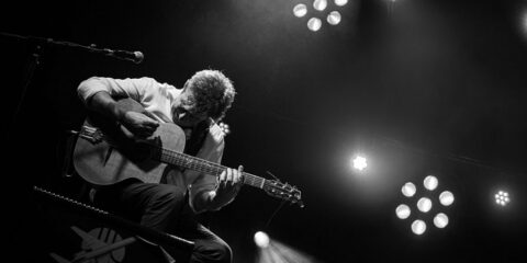 Musicien jouant de la guitare sur scène en noir et blanc.