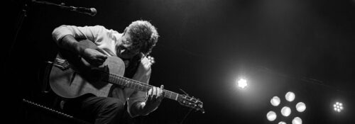 Musicien jouant de la guitare sur scène en noir et blanc.