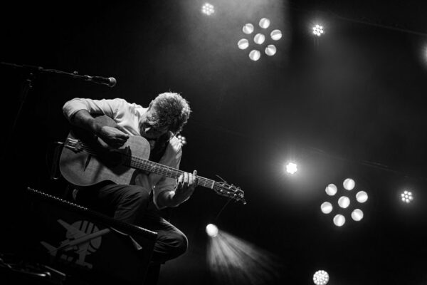 Musicien jouant de la guitare sur scène en noir et blanc.