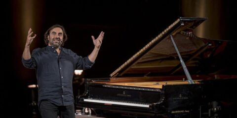 Homme souriant devant un piano à queue.