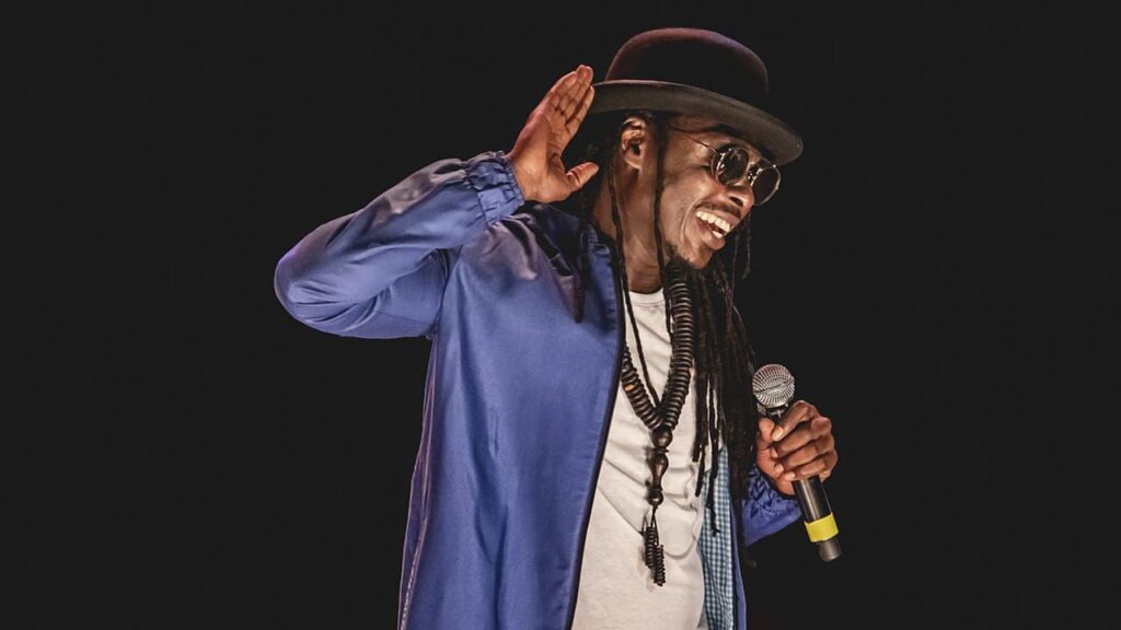 Homme avec micro et chapeau sur scène.