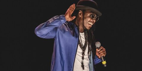 Homme avec micro et chapeau sur scène.