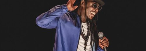 Homme avec micro et chapeau sur scène.