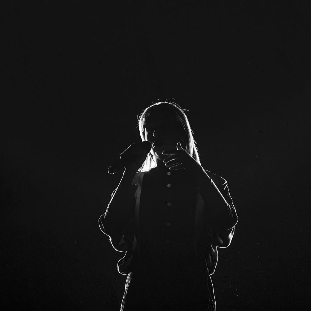 Chanteur silhouette avec microphone sur scène sombre.