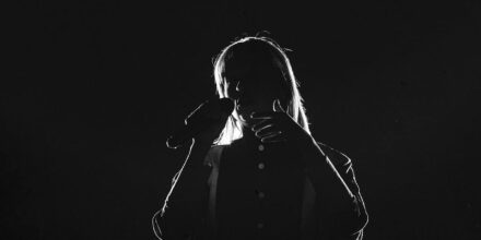 Chanteur silhouette avec microphone sur scène sombre.