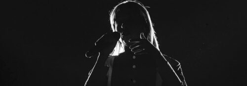 Chanteur silhouette avec microphone sur scène sombre.