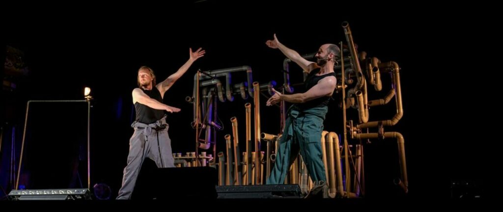 Deux artistes sur scène avec décor de tuyaux.