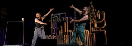 Deux artistes sur scène avec décor de tuyaux.
