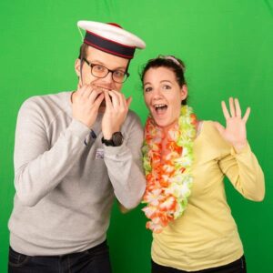 Deux personnes souriantes posent devant un fond vert.