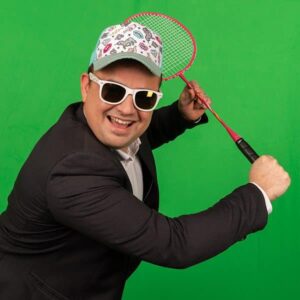 Homme en costume, jouant badminton, fond vert.